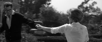 Movie still from “The Gazebo” (1959), directed by George Marshall – Two people holding hands in front of a car in a black and white photo; Medium shot, Over the shoulder angle