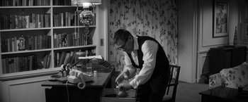 Movie still from “The Gazebo” (1959), directed by George Marshall – A man in a suit and tie working in a cluttered room; Medium shot, High angle