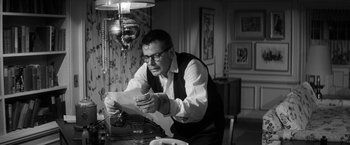 Movie still from “The Gazebo” (1959), directed by George Marshall – A man sitting at a table looking at a piece of paper; Medium shot, High angle