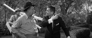 Movie still from “The Gazebo” (1959), directed by George Marshall – A man in a suit and tie is pulling another man's tie; Medium shot, Over the shoulder angle