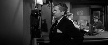 Movie still from “The Gazebo” (1959), directed by George Marshall – Black and white photograph of a man in a suit and tie in front of a video camera; Close Up shot, Low angle