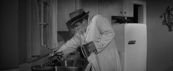 Movie still from “The Gazebo” (1959), directed by George Marshall – A man in a hat is washing dishes in a kitchen; Medium shot, High angle