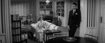 Movie still from “The Gazebo” (1959), directed by George Marshall – A man and a woman are sitting on a couch; Wide shot, Over the shoulder angle