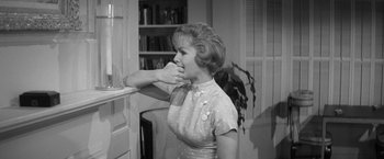 Movie still from “The Gazebo” (1959), directed by George Marshall – A black - and - white photo of a woman looking at a book; Medium shot, Over the shoulder angle