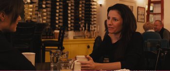 Movie still from “The Girlfriend Experience” (2009), directed by Steven Soderbergh – A woman sitting at a table in front of a wine rack; Medium shot, Over the shoulder angle