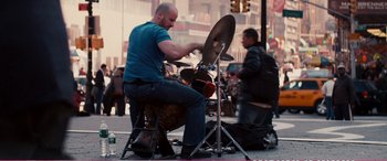 Movie still from “The Girlfriend Experience” (2009), directed by Steven Soderbergh – A man sitting on top of a drum set on the street; Wide shot, Low angle