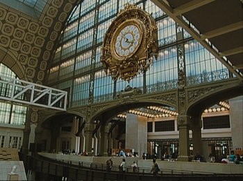 Movie still from “The Gleaners & I” (2000), directed by Agnès Varda – A large clock hanging from the side of a building; Extreme Wide shot, Low angle