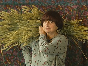 Movie still from “The Gleaners & I” (2000), directed by Agnès Varda – A woman holding a bundle of wheat over her head; Medium shot, Low angle