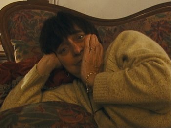 Movie still from “The Gleaners & I” (2000), directed by Agnès Varda – A woman laying on a couch talking on a phone; Medium shot, High angle