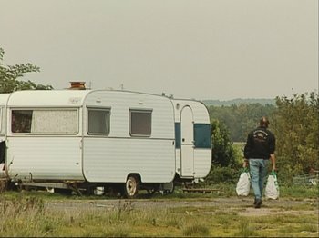 Movie still from “The Gleaners & I” (2000), directed by Agnès Varda – A man walking in front of an old trailer; Wide shot, Low angle