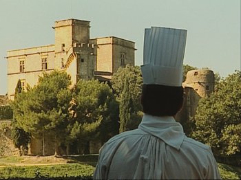 Movie still from “The Gleaners & I” (2000), directed by Agnès Varda – A man wearing a chef's hat standing in front of a castle; Extreme Wide shot, Low angle