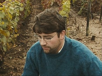 Movie still from “The Gleaners & I” (2000), directed by Agnès Varda – A man wearing glasses and a blue sweater in a vineyard; Close Up shot, High angle