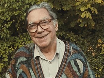 Movie still from “The Gleaners & I” (2000), directed by Agnès Varda – An older man wearing glasses and a colorful sweater; Close Up shot, High angle