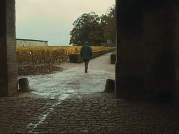 Movie still from “The Gleaners & I” (2000), directed by Agnès Varda – A person walking down a brick path near a field; Wide shot, High angle