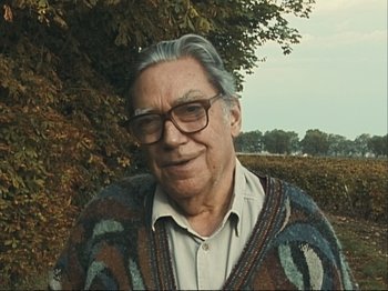 Movie still from “The Gleaners & I” (2000), directed by Agnès Varda – An older man wearing glasses and wearing a sweater; Close Up shot, Low angle