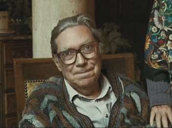 Movie still from “The Gleaners & I” (2000), directed by Agnès Varda – An older man wearing glasses sitting in a chair; Close Up shot, High angle