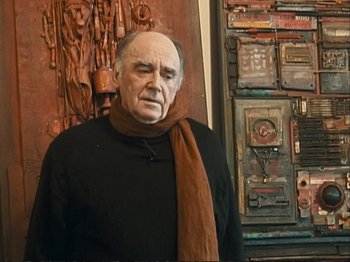 Movie still from “The Gleaners & I” (2000), directed by Agnès Varda – An older man wearing a black shirt and a brown scarf; Medium shot, Low angle