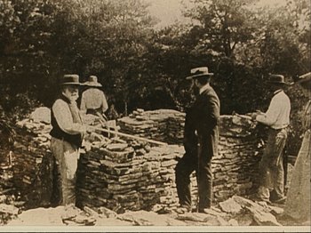 Movie still from “The Gleaners & I” (2000), directed by Agnès Varda – A group of men standing next to a pile of rocks; Wide shot, Low angle