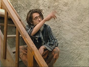 Movie still from “The Gleaners & I” (2000), directed by Agnès Varda – A man sitting on the steps of a wooden stair case; Medium shot, High angle