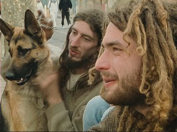 Movie still from “The Gleaners & I” (2000), directed by Agnès Varda – Two men and a dog are sitting on the sidewalk; Close Up shot, Low angle