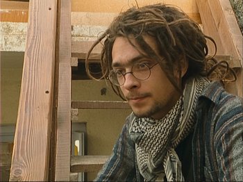 Movie still from “The Gleaners & I” (2000), directed by Agnès Varda – A man with dreads sitting on some steps; Close Up shot, Low angle