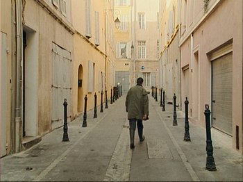Movie still from “The Gleaners & I” (2000), directed by Agnès Varda – A man walking down a street in the middle of the day; Wide shot, High angle
