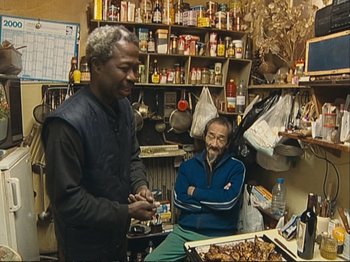 Movie still from “The Gleaners & I” (2000), directed by Agnès Varda – Two men are sitting in a room with food; Medium shot, High angle
