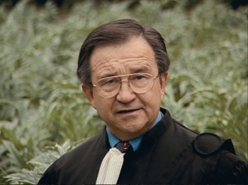 Movie still from “The Gleaners & I” (2000), directed by Agnès Varda – An older man wearing a suit and tie in front of some bushes; Close Up shot, High angle