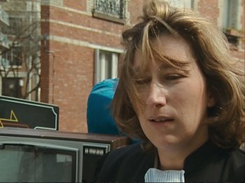 Movie still from “The Gleaners & I” (2000), directed by Agnès Varda – A person wearing a suit near a brick building; Close Up shot, High angle