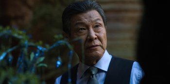 Movie still from “Altered Carbon” (2018), created by Laeta Kalogridis – An older asian man wearing a suit and tie; Close Up shot, Low angle