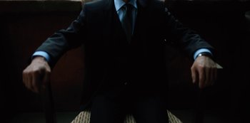 Movie still from “Altered Carbon” (2018), created by Laeta Kalogridis – A man wearing a suit and tie sitting on a chair; Medium shot, High angle