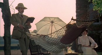 Movie still from “The Go-Between” (1971), directed by Joseph Losey – A person holding an open umbrella while reading a book; Wide shot, Low angle