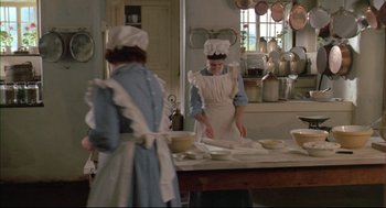 Movie still from “The Go-Between” (1971), directed by Joseph Losey – Two women dressed in aprons in a kitchen preparing food; Wide shot, High angle