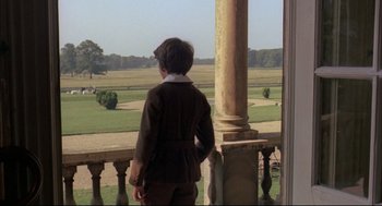 Movie still from “The Go-Between” (1971), directed by Joseph Losey – A young boy standing on a porch looking out at a field; Wide shot, Over the shoulder angle