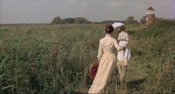 Movie still from “The Go-Between” (1971), directed by Joseph Losey – Two women are walking through a field with an umbrella; Extreme Wide shot, High angle