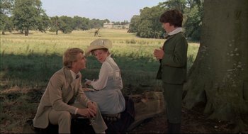 Movie still from “The Go-Between” (1971), directed by Joseph Losey – A man and two women and a boy are sitting in a field; Medium shot, Over the shoulder angle