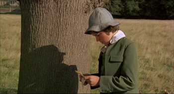 Movie still from “The Go-Between” (1971), directed by Joseph Losey – A young boy wearing a hat looking down at a leaf; Medium shot, High angle