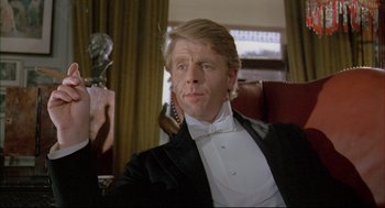 Movie still from “The Go-Between” (1971), directed by Joseph Losey – A man in a tuxedo sitting in front of a microphone; Close Up shot, Low angle