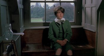 Movie still from “The Go-Between” (1971), directed by Joseph Losey – A young boy sitting on top of a wooden bench in front of a window; Medium shot, High angle