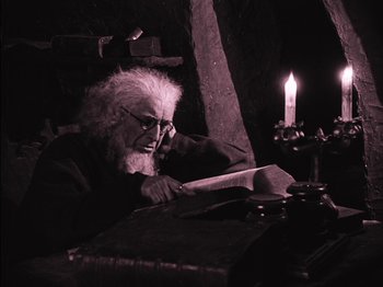 Movie still from “The Golem” (1920), directed by Paul Wegener – An old man sitting at a table reading a book by a candle; Medium shot, Low angle