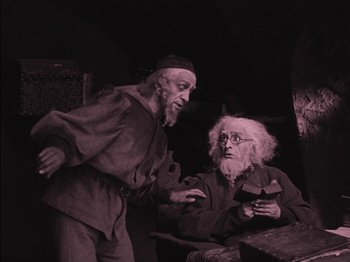 Movie still from “The Golem” (1920), directed by Paul Wegener – Two old men are talking in a dark room; Medium shot, High angle
