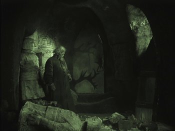 Movie still from “The Golem” (1920), directed by Paul Wegener – An old man standing in a dark cave; Wide shot, Low angle