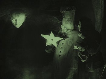 Movie still from “The Golem” (1920), directed by Paul Wegener – A person in a costume holding a star; Medium shot, Low angle