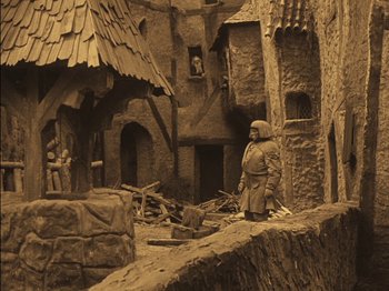 Movie still from “The Golem” (1920), directed by Paul Wegener – A statue of a man standing next to a building; Wide shot, High angle