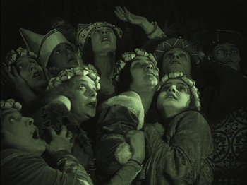 Movie still from “The Golem” (1920), directed by Paul Wegener – A group of people in a dark room singing together; Medium shot, High angle