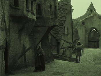 Movie still from “The Golem” (1920), directed by Paul Wegener – Two people are standing in front of an old building; Wide shot, High angle