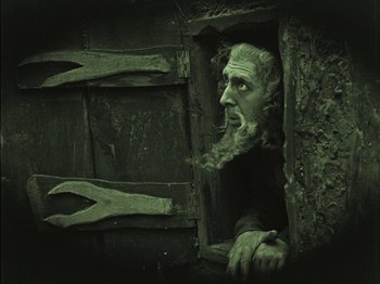 Movie still from “The Golem” (1920), directed by Paul Wegener – An old man with long hair and a long beard looking out of an open door; Medium shot, Low angle