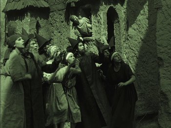 Movie still from “The Golem” (1920), directed by Paul Wegener – A group of people dressed as witches standing in front of a stone wall; Wide shot, High angle