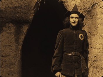 Movie still from “The Golem” (1920), directed by Paul Wegener – A man dressed as a wizard standing in front of a cave; Medium shot, High angle
