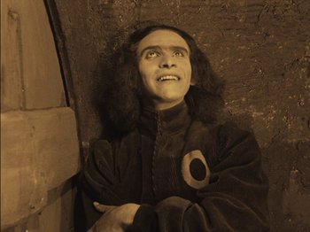 Movie still from “The Golem” (1920), directed by Paul Wegener – A man with long black hair is smiling; Medium shot, High angle